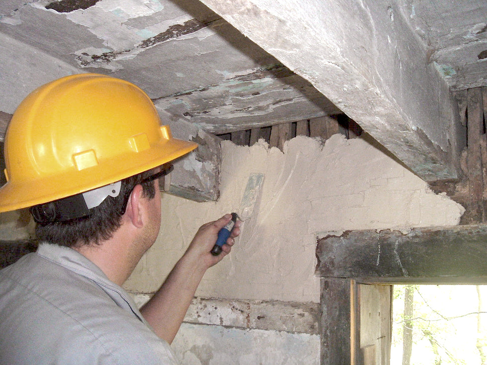 Person in a yellow hard hat applying plaster to a ceiling.