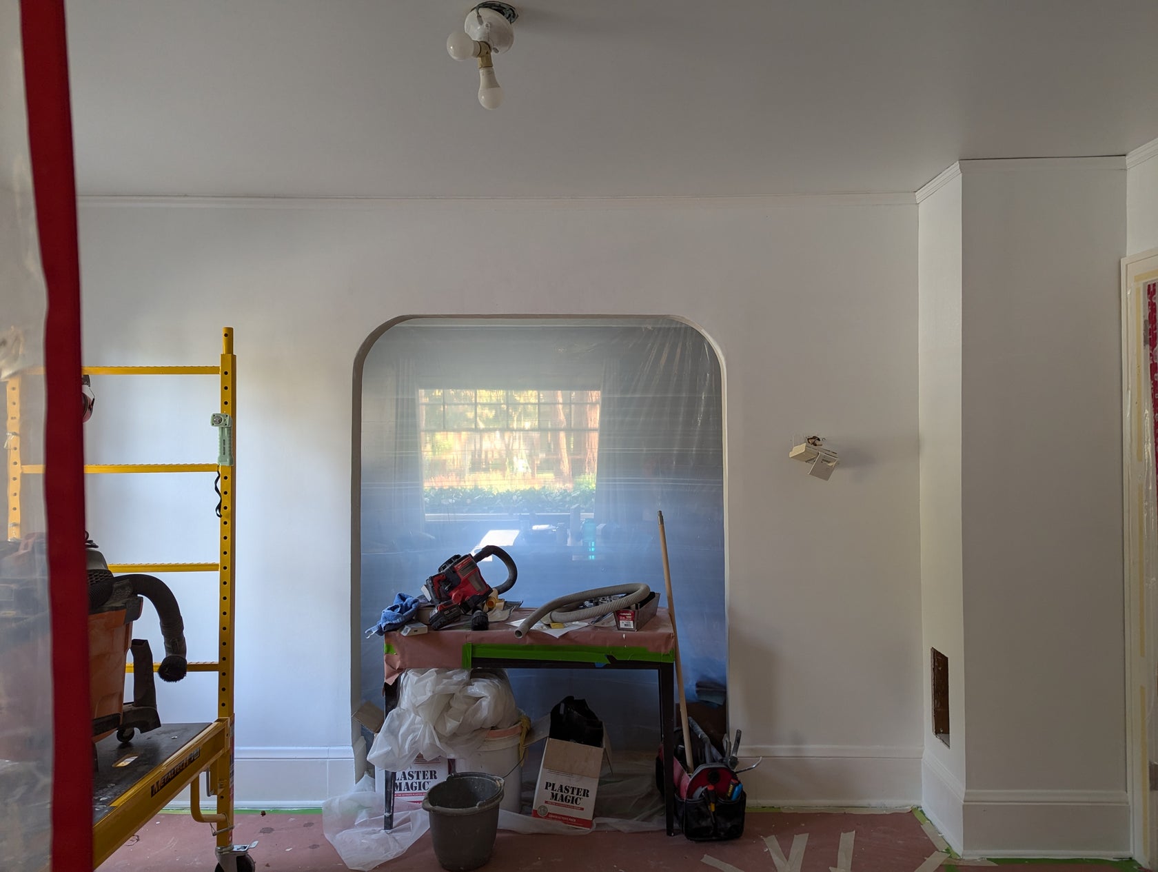 Room with white walls, a ladder, and various items on a table.