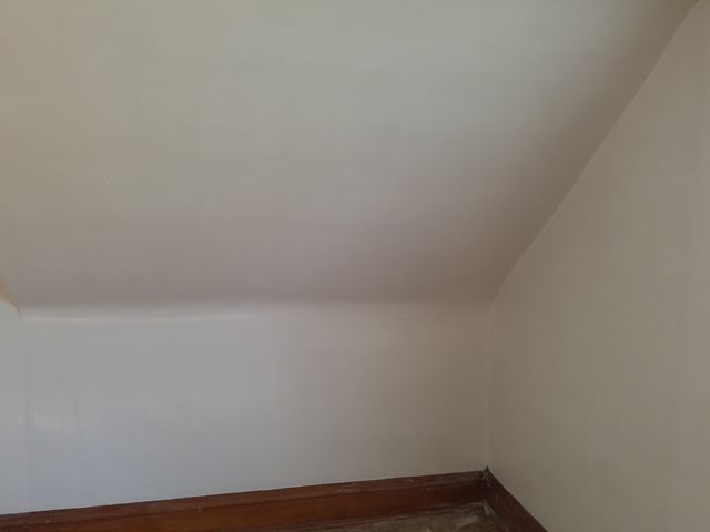 Corner of a room with white walls and a wooden baseboard.

