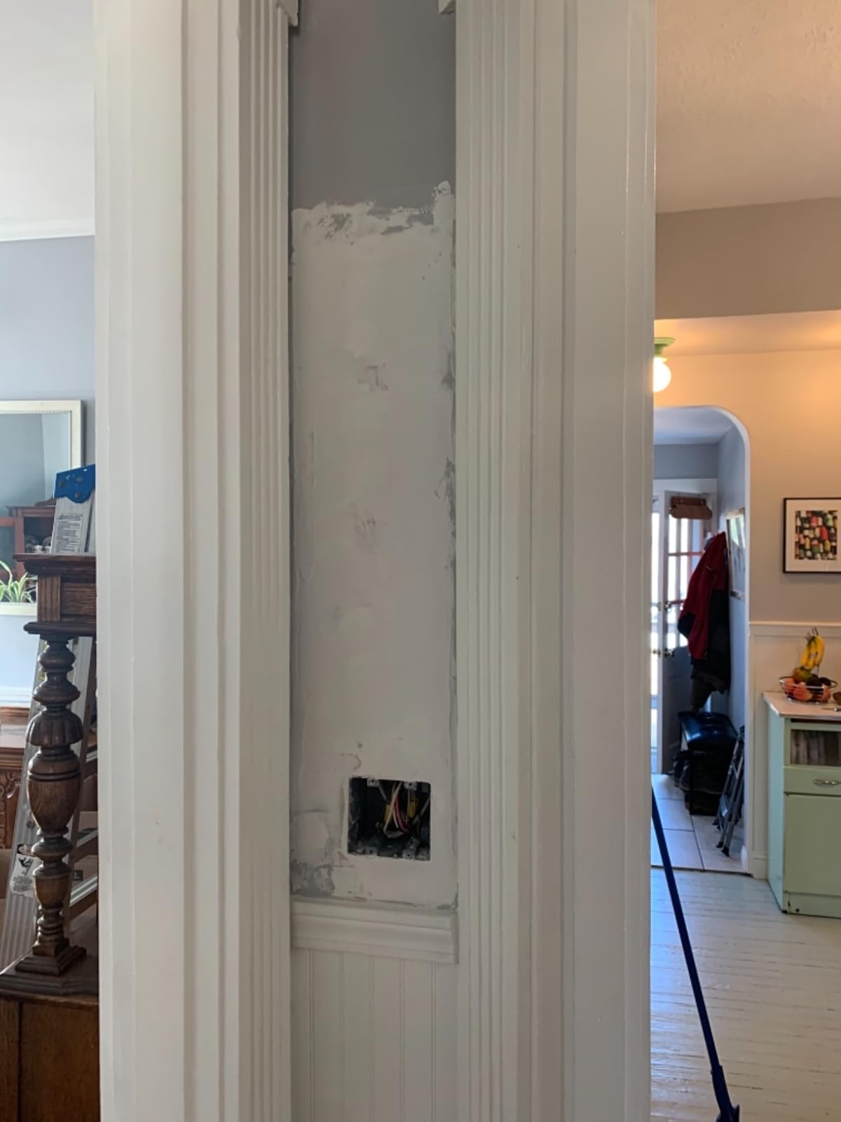 Partially repaired plaster section beside an interior doorway with original wood trim.