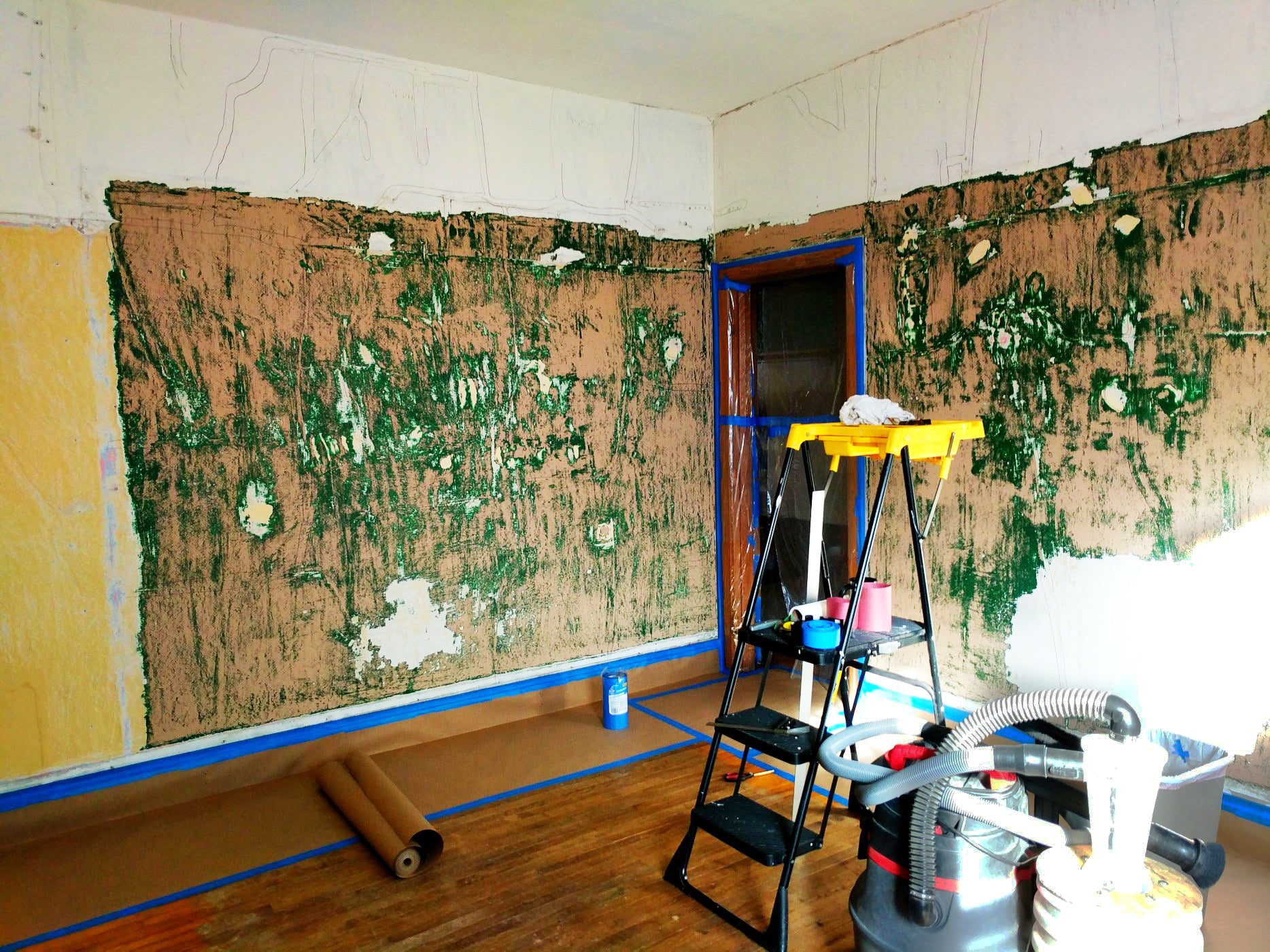 Room under renovation with peeling wallpaper, ladder, and cleaning equipment.