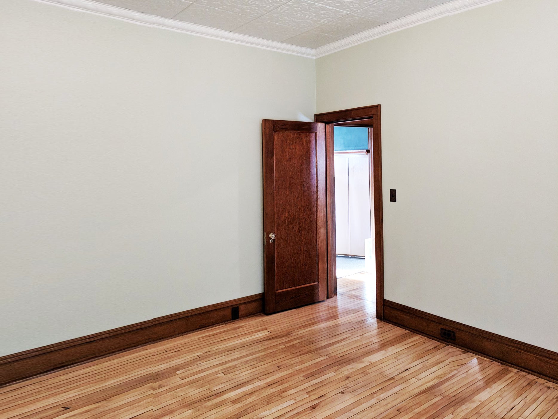 Empty room with wooden floor and open door leading to another room.