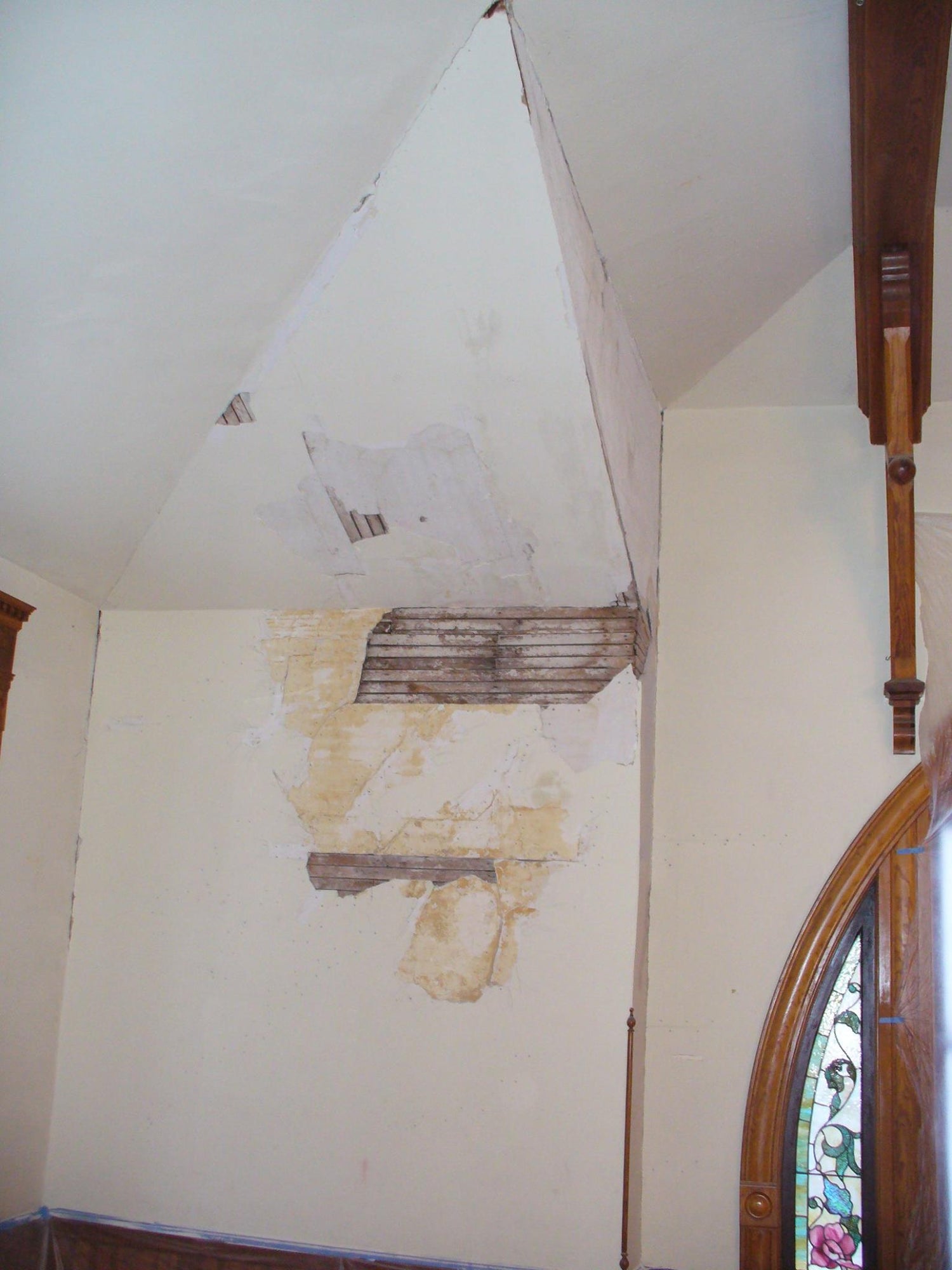Damaged plaster ceiling and wall exposing wooden lath in a historic room near an arched window