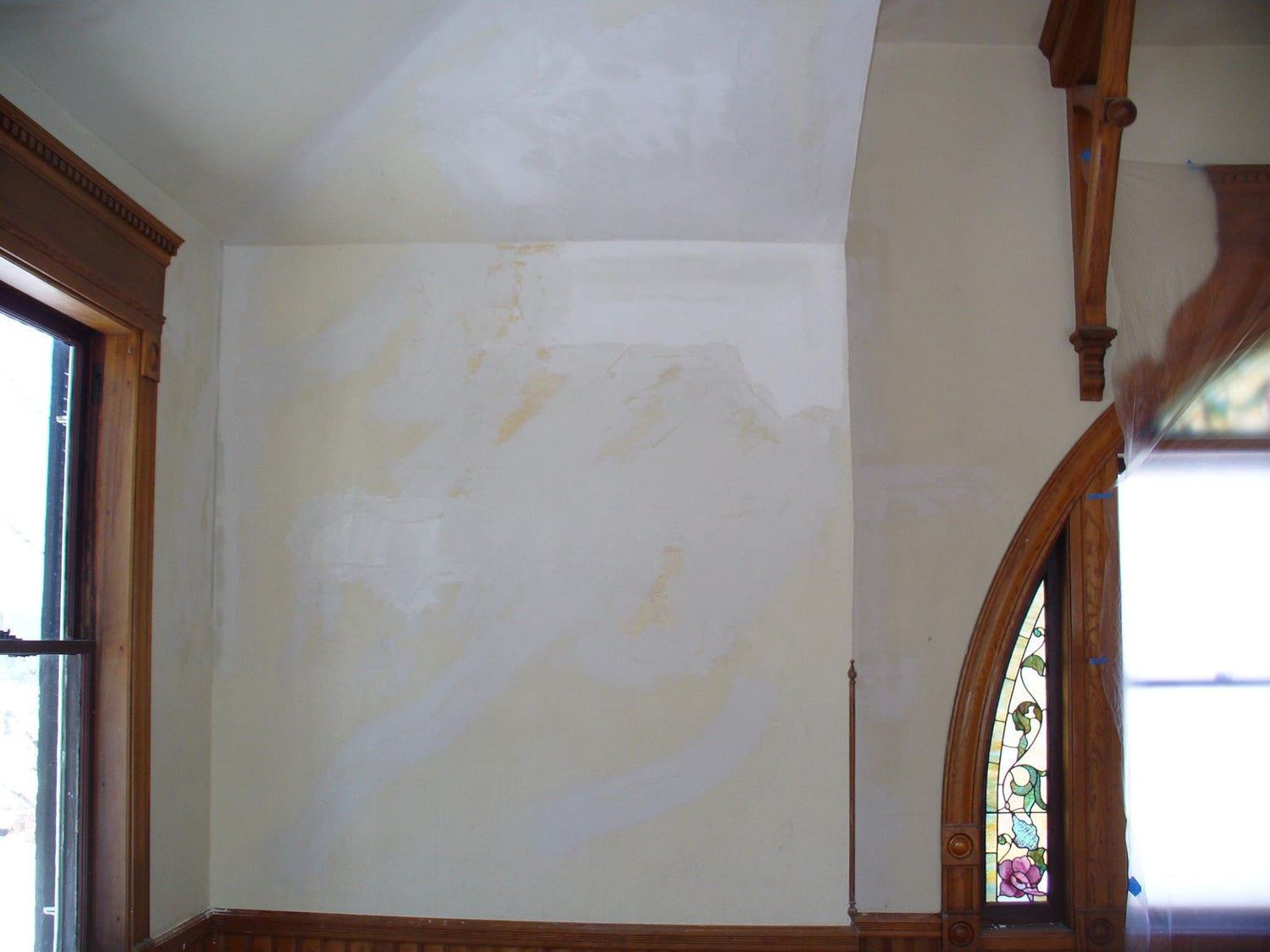 Partially restored plaster wall in a historic room, showing repaired sections around wooden trim and arched window