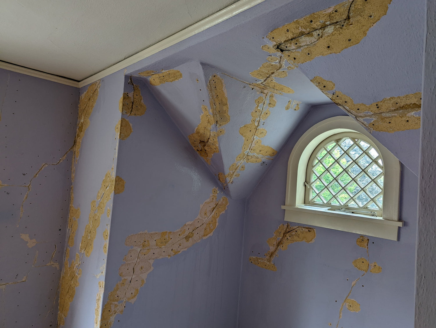 Historic room with extensive plaster delamination and exposed substrate around an arched window.