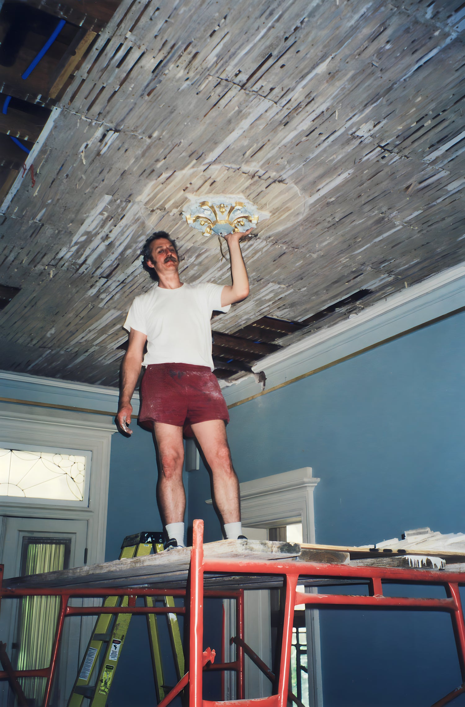 Person on a ladder repairing a ceiling with tools