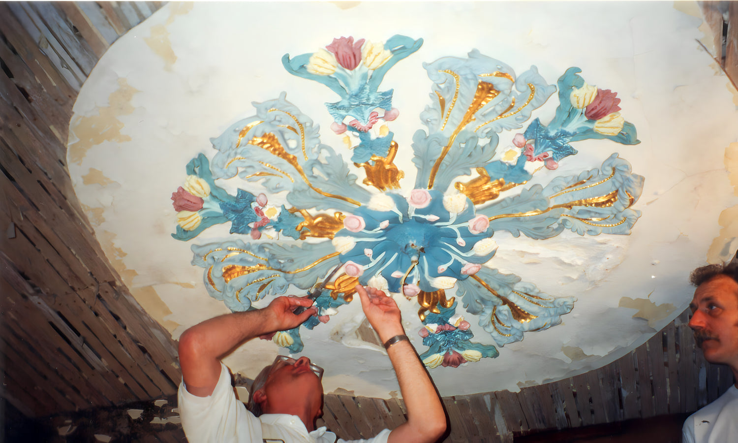 Person working on a decorative ceiling fresco with floral and leaf patterns.