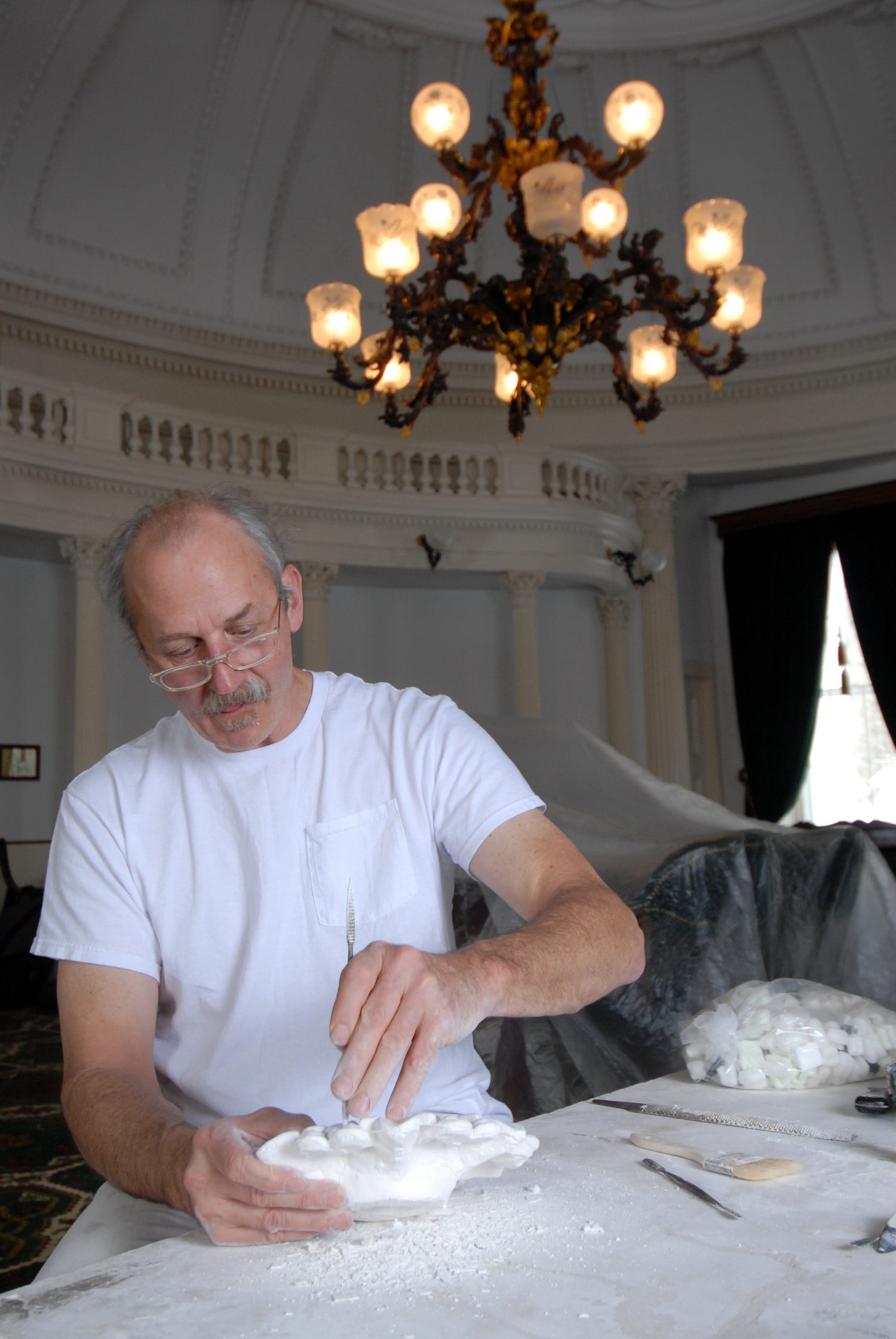 Man working with white material on a table under a chandelier