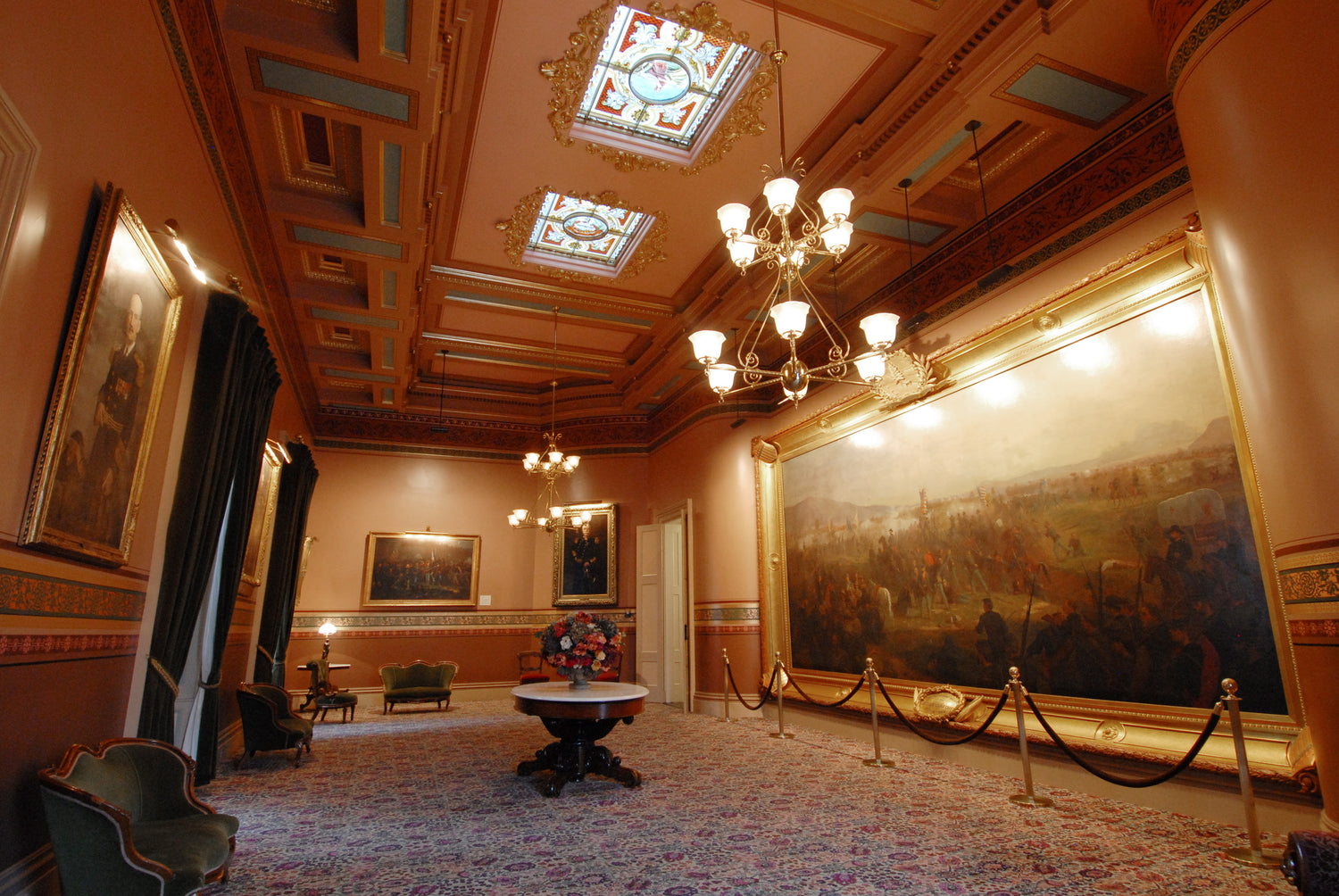 Opulent room with classical decor, including a chandelier, paintings, and a large mural.