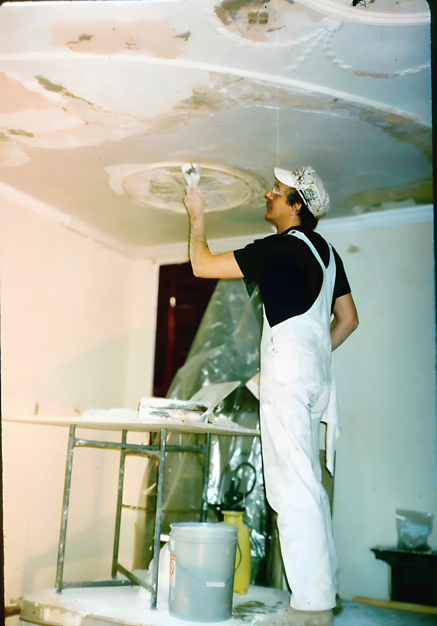 Person installing drywall on a ceiling in a room under renovation.