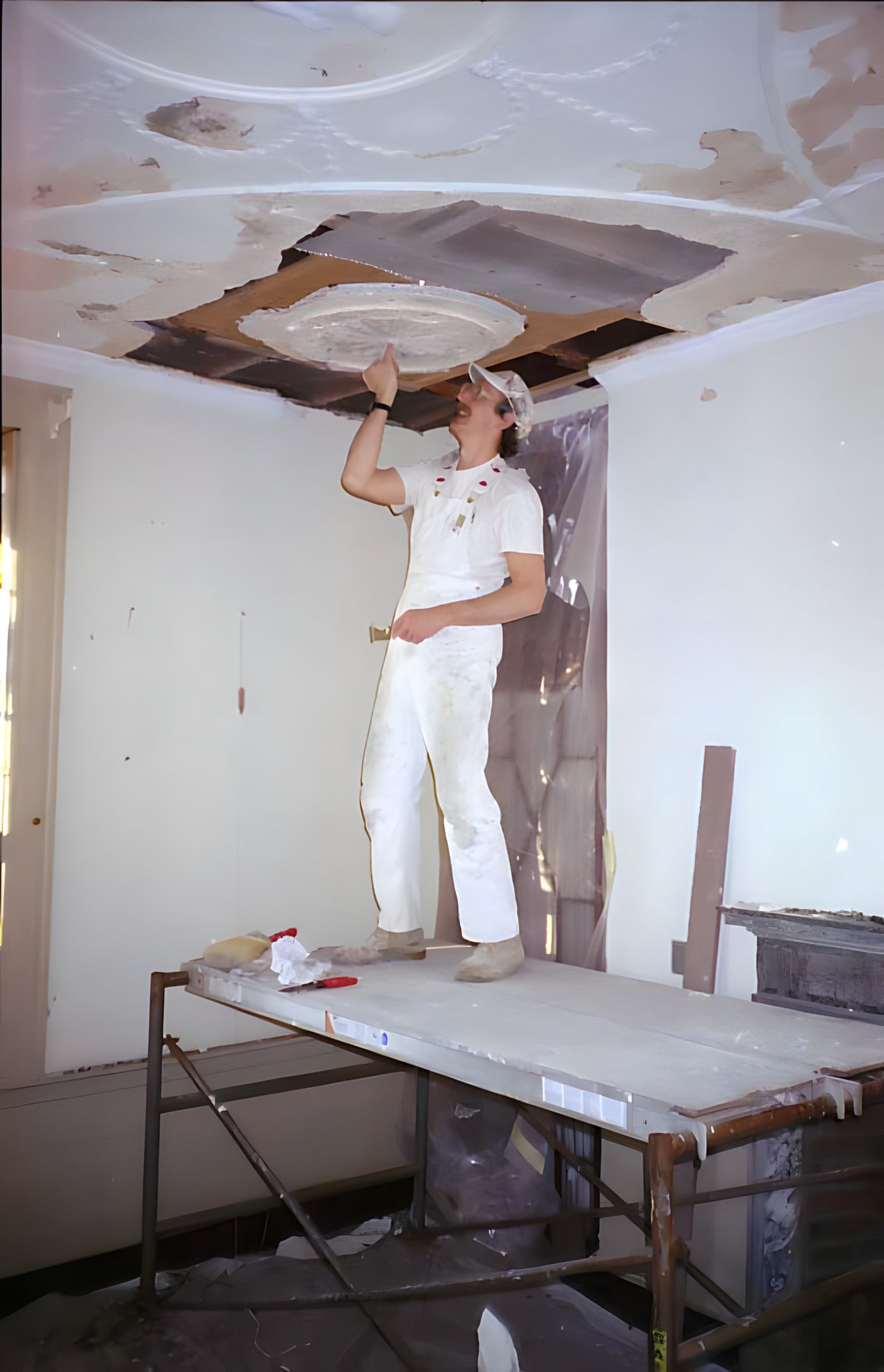 Person on a ladder working on a ceiling repair in a room with white walls.