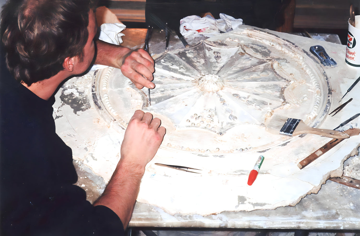 Person working on a large circular object with tools and materials around
