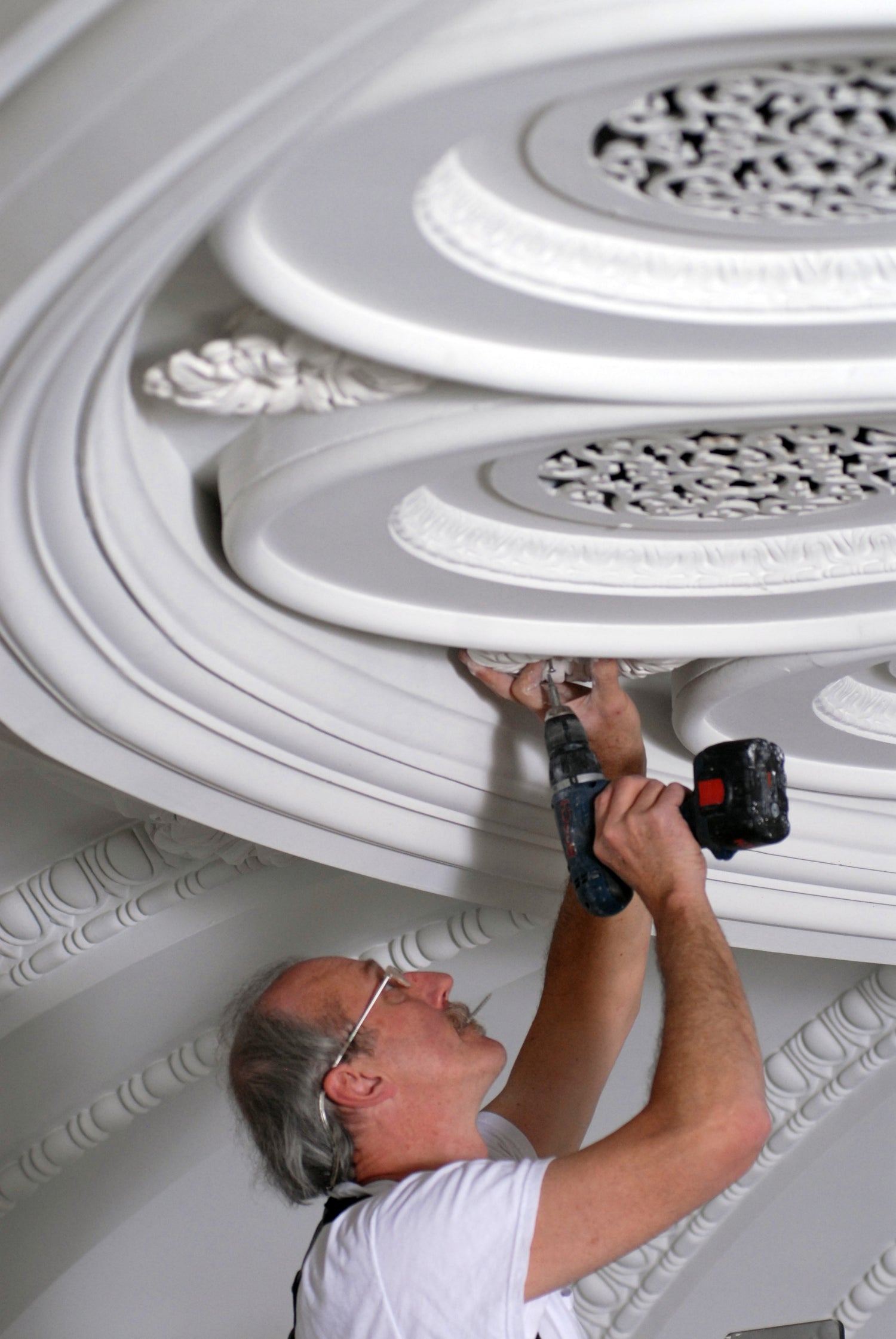 Person installing decorative ceiling molding with a tool.
