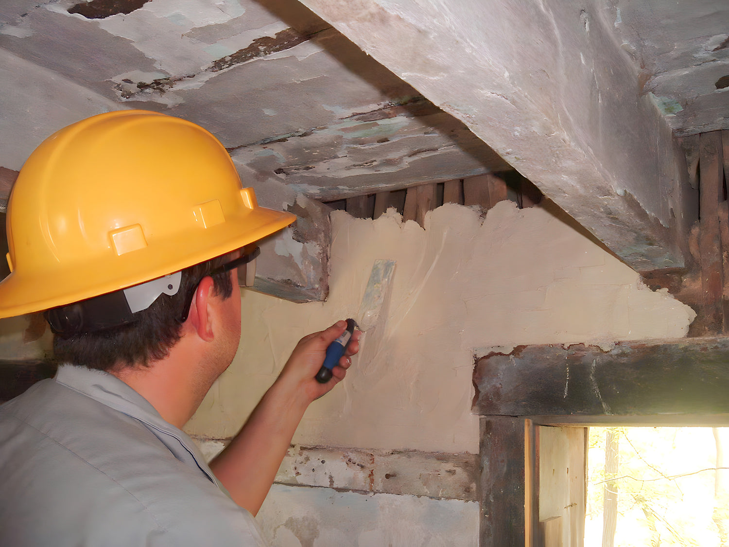 Person in a hard hat applying plaster to a ceiling