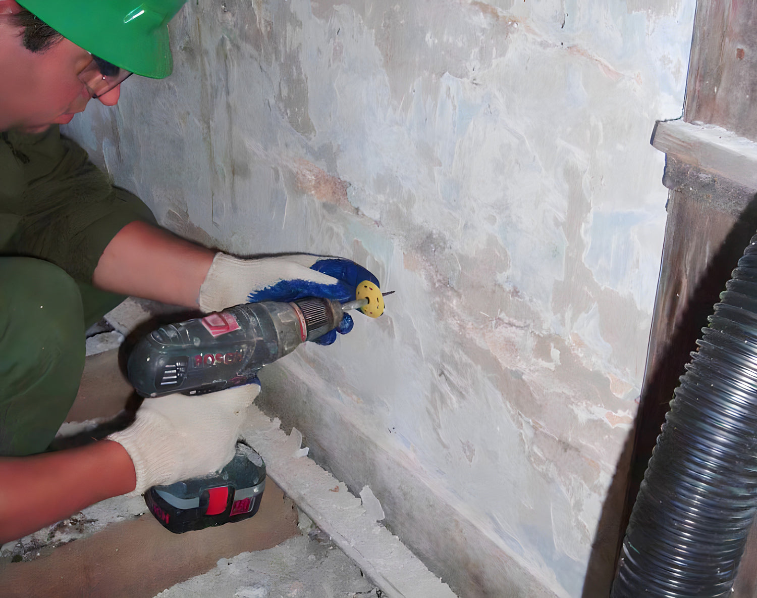 Person using a drill on a wall with visible pipes and tools.