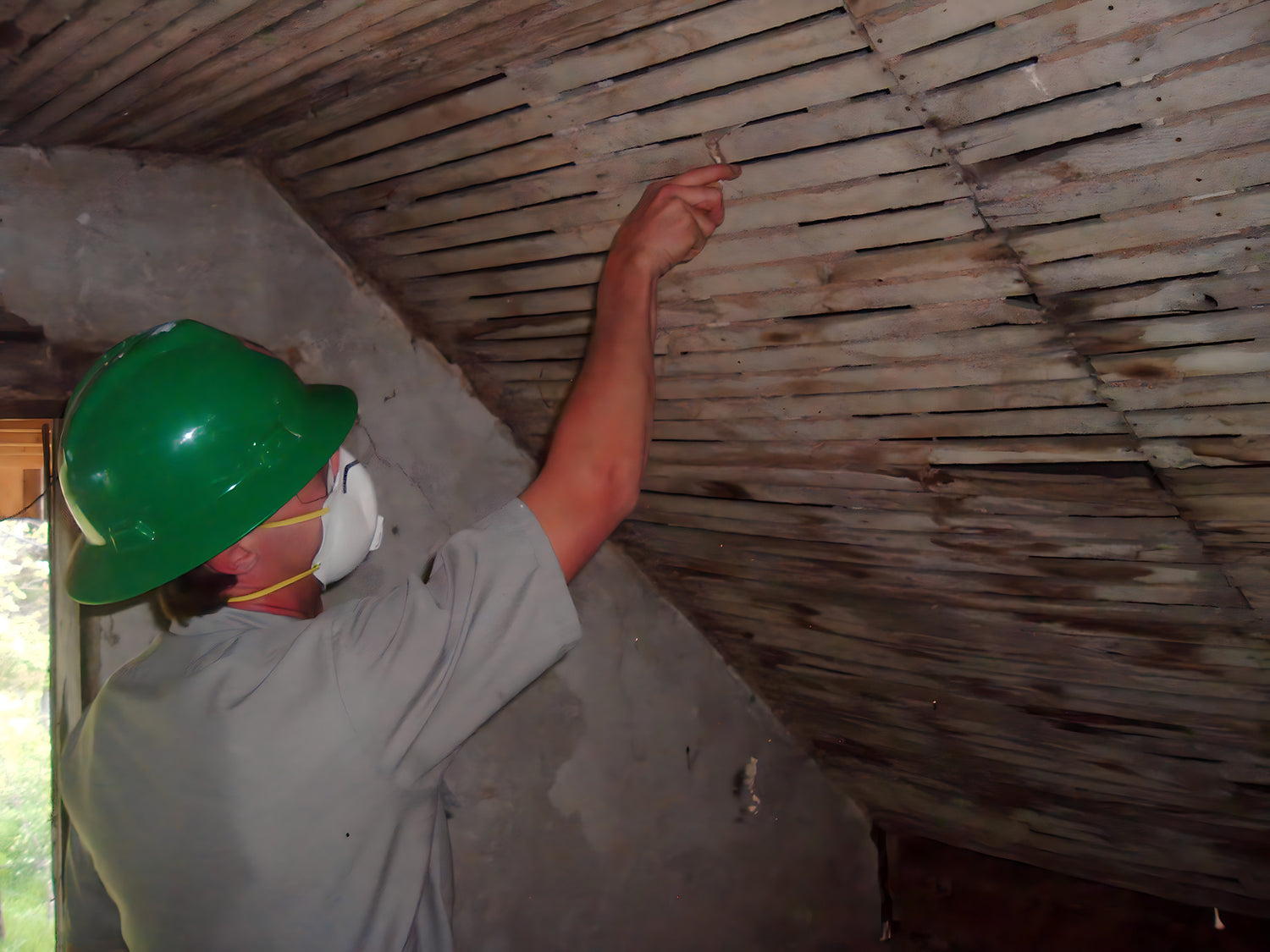 Person wearing a green helmet and white gloves working on a wooden ceiling.