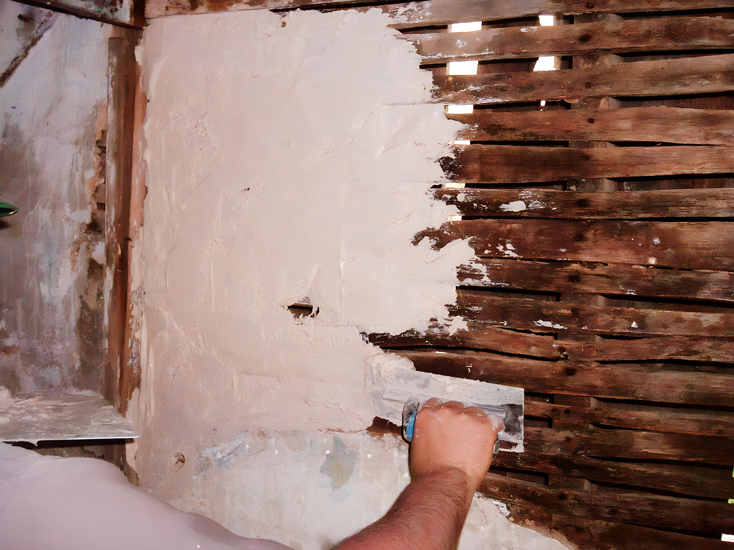 Person applying plaster to a wall with a trowel, next to a wooden panel.