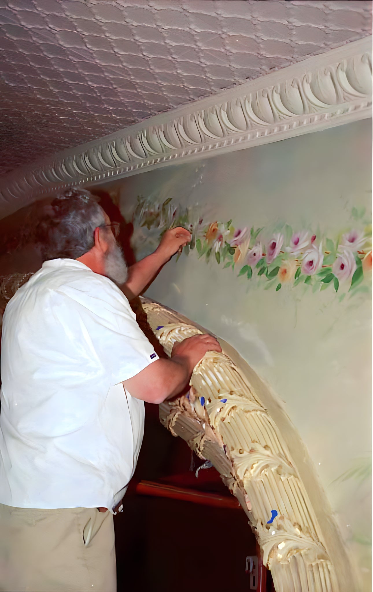 Person applying decorative floral design to a wall with a decorative cornice.