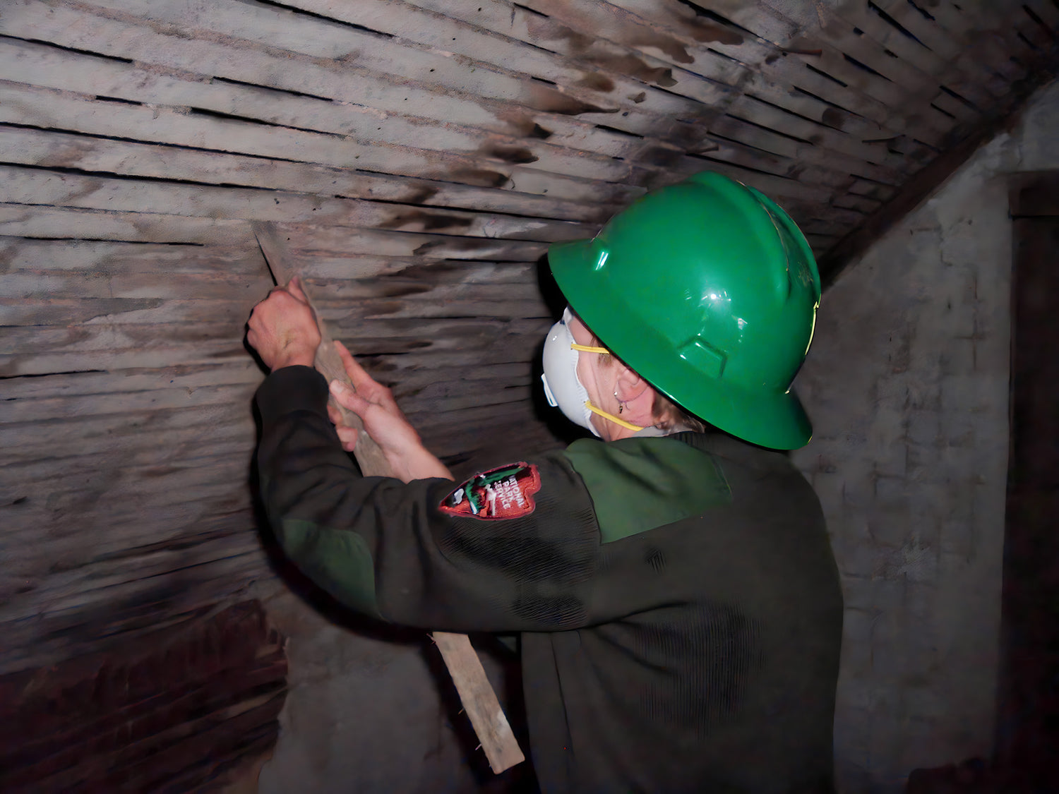 Person in a green hard hat and safety goggles working on a ceiling.