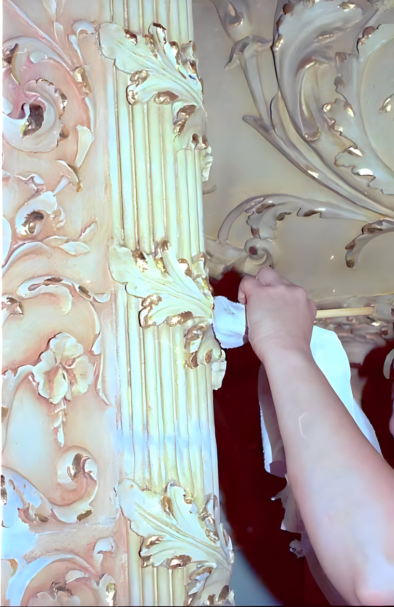 Decorative ceiling with intricate carvings and a hand applying white paint.