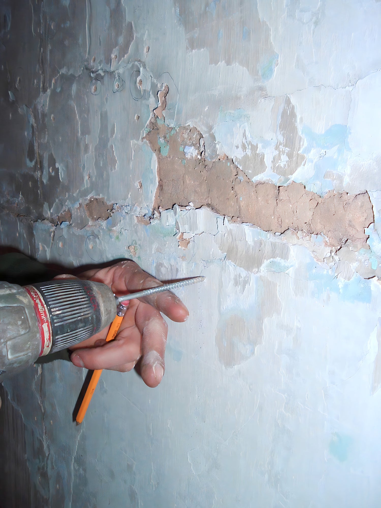 Hand using a drill on a wall with peeling paint