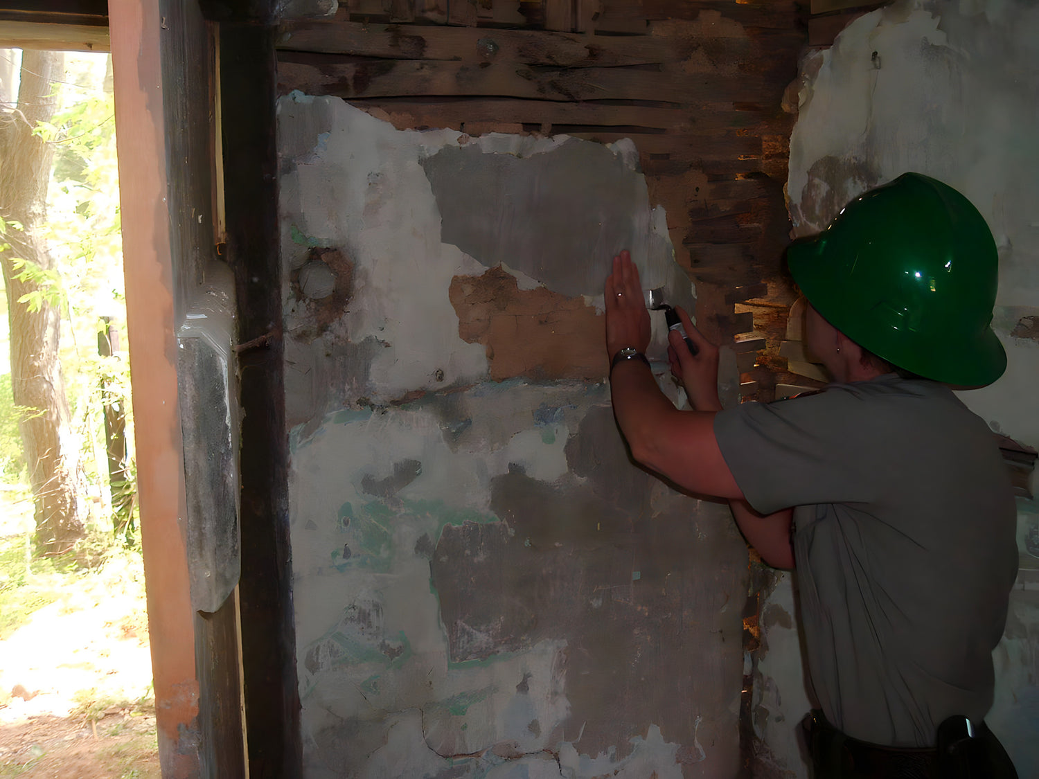Person in a green hard hat working on a wall inside a building.